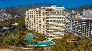 A multi-story hotel with balconies, a swimming pool, and a view of the surrounding city and hills.