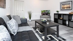 Een moderne woonkamer met een zwarte leren bank, een salontafel, een televisie en een boekenplank.