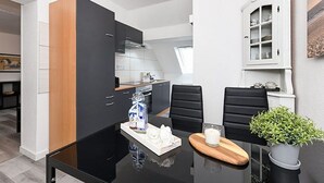 Een moderne keuken met zwarte en houten kastjes, een eettafel met stoelen, en een potplant.