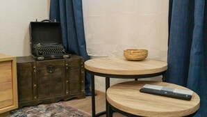 Et værelse med en vintageskuffe, et lille rundt bord med en fjernbetjening og en flettet kurv.
