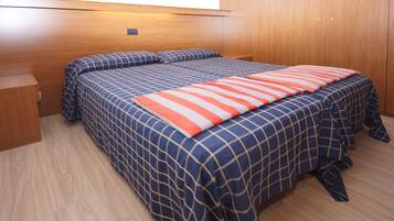 Ein Schlafzimmer mit einem Holz-Kopfstück, zwei Betten mit blau-orangenem Bettbezug, einem Nachttisch aus Holz und einem Kleiderschrank.