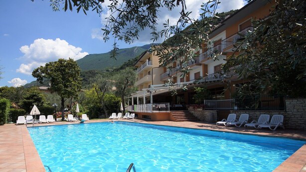 Une piscine à l’eau d’un bleu cristallin, entourée de chaises longues blanches et bordée d’un bâtiment doté de balcons.