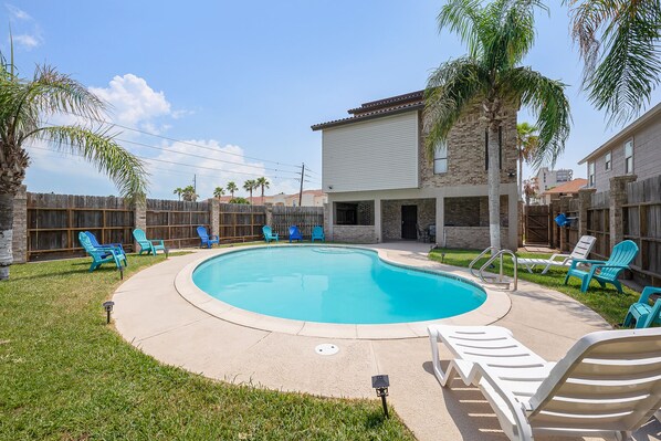 Ein Garten mit Swimmingpool, blauen und weißen Liegestühlen und einem Holzzaun.