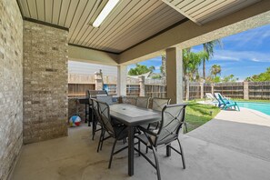Eine Außenpatio mit einer Ziegelwand, einem Tisch mit Stühlen, einem Grill und einem Pool im Hintergrund.