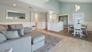 Ein geräumiges Wohnzimmer mit einem grauen Ecksofa, einem Essbereich mit weißem Tisch und Stühlen sowie einer Küche im Hintergrund.