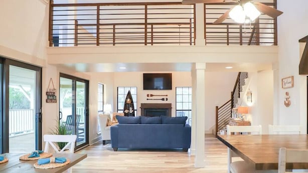 A spacious living area with a blue sofa, a wooden dining table, and a staircase leading to a balcony.