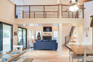 A spacious living area with a blue sofa, a wooden dining table, and a staircase leading to a balcony.