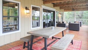 A covered outdoor area with a wooden deck, a dining table with benches, and a seating area with sofas.