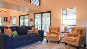 A living room with a dark blue sofa, beige armchairs, a patterned rug, and a large window with a view.