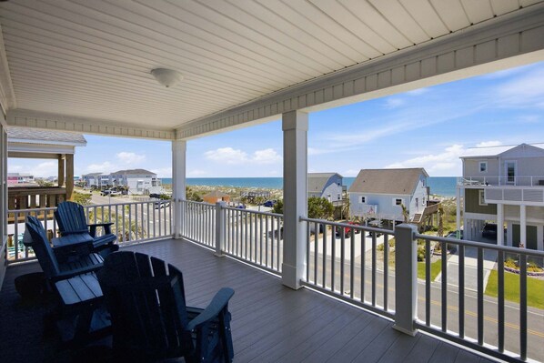 A covered porch with Adirondack chairs, a view of the ocean, and neighboring houses.