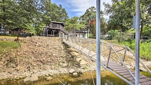 Eine Holzbrücke über einen steinigen Flussufer, die zu einem Gebäude mit einer Treppe führt.