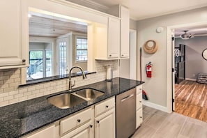 A kitchen with white cabinets, a black countertop, and a stainless steel sink. There is a fire extinguisher on the wall and a wicker basket hanging on the wall.