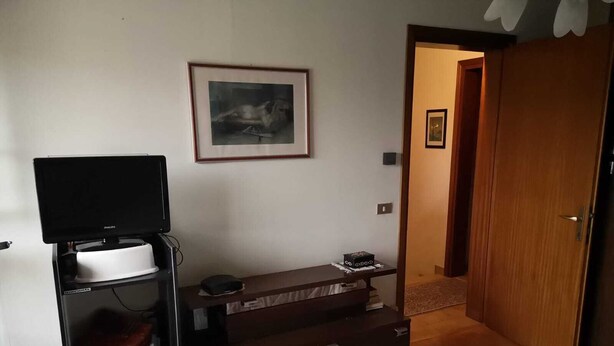 A bedroom with a bed, a TV stand with a television, a dresser, and a framed picture on the wall.