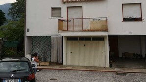 A two-story building with a garage, a balcony with a metal railing, and a car parked in front.