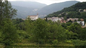A hillside village with buildings, including a church with a bell tower, surrounded by lush greenery.