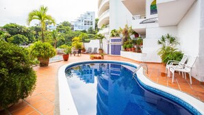 A swimming pool surrounded by potted plants and outdoor seating.