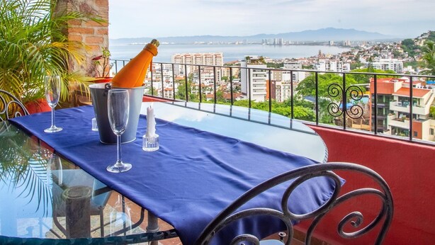 A balcony with a table set for two, a bottle of champagne, and a view of the cityscape.