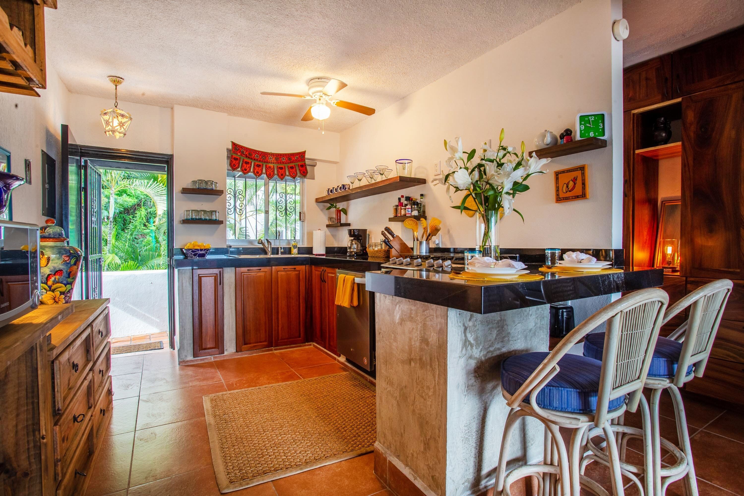 Una cocina con una isla central, armarios de madera y un comedor con sillas de mimbre.