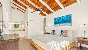 A bedroom with a wooden ceiling, a bed with a white bedspread, a nightstand with a lamp, and a painting of the ocean on the wall. - Beautiful 2 Br 2.5 Ba Condo Golf Course View, Pool, Hot Tub (209AB) (Princeville)