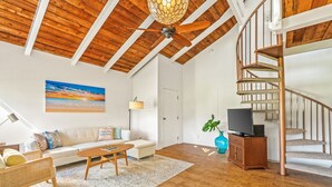 A spacious living room with a wooden ceiling, a large painting, a sofa, a coffee table, and a staircase. - Beautiful 2 Br 2.5 Ba Condo Golf Course View, Pool, Hot Tub (209AB) (Princeville)