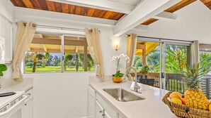 A kitchen with a large window, white cabinets, a stainless steel sink, and a fruit basket on the counter. - Beautiful 2 Br 2.5 Ba Condo Golf Course View, Pool, Hot Tub (209AB) (Princeville)