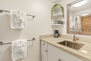 A modern bathroom with a sink, countertop, and towel rack. - Bright and Beautiful Princeville Studio, Private Lanai, Pool (209B) (Princeville)