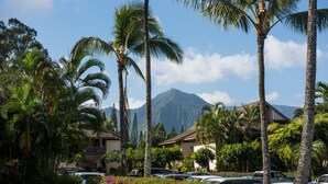 A resort with palm trees, a mountain in the background, and cars parked in the lot. - Bright and Beautiful Princeville Studio, Private Lanai, Pool (209B) (Princeville)