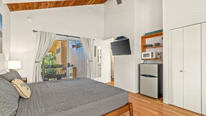 A bedroom with a bed, a TV, a microwave, and a small kitchenette. - Bright and Beautiful Princeville Studio, Private Lanai, Pool (209B) (Princeville)