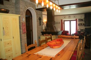 A dining area with a wooden table, chairs, a woven basket, and a stone wall. - Panfili House (Umbria)