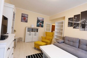 Un salon avec un canapé, un fauteuil jaune, un meuble blanc et un téléviseur.