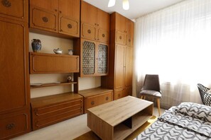 Une chambre à coucher avec des meubles en bois, un lit, une chaise et une fenêtre ornée de rideaux légers.