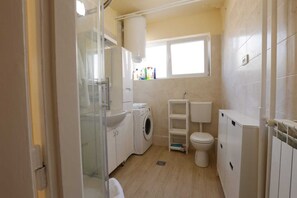 Une petite salle de bain équipée d’un lave-linge, de toilettes et d’une petite fenêtre pour laisser entrer la lumière naturelle.