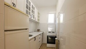 Une cuisine compacte avec des meubles blancs, un four encastré et une fenêtre qui laisse entrer la lumière naturelle.