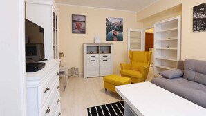 Un salon moderne avec un canapé, un fauteuil jaune, un téléviseur et un meuble blanc.