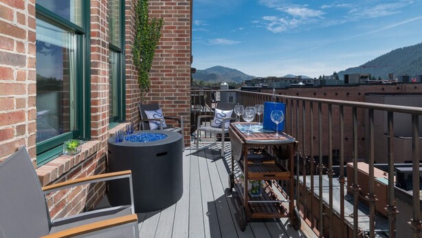 A rooftop deck with outdoor seating, a fire pit, and a view of the cityscape and mountains. - Private Balcony | Firepit | Portable Bar (Ketchum)