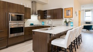 A modern kitchen with dark wood cabinets, stainless steel appliances, a central island with bar stools, and a large window providing natural light. - Private Balcony | Firepit | Portable Bar (Ketchum)
