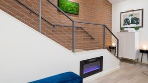 A staircase with a brick wall, a flat-screen TV, a framed picture, and a white cabinet with a small table and a plant. - Private Balcony | Firepit | Portable Bar (Ketchum)