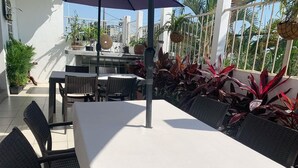 Um pátio externo com uma mesa e cadeiras, cercado por vasos de plantas e vista para a cidade.