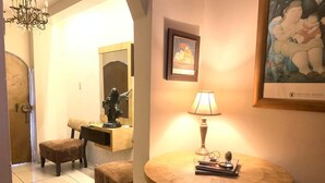 Um corredor bem iluminado com uma mesa redonda de madeira, uma luminária e um quadro na parede.
