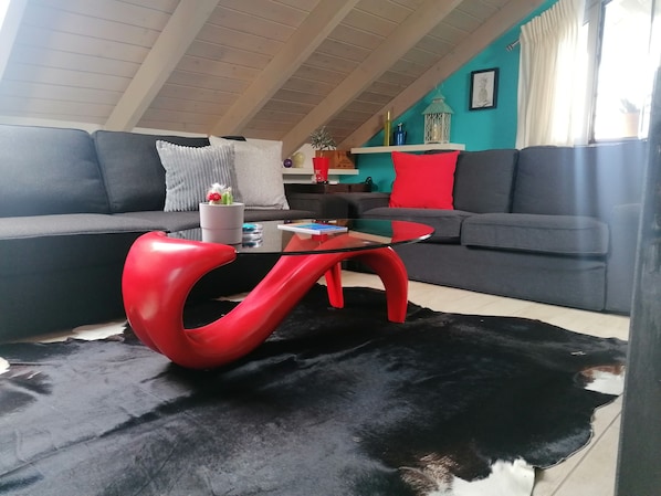 A modern living room with a black and red glass coffee table, grey sofas, and a black cowhide rug.