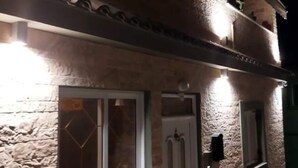 Ein zweistöckiges Gebäude mit einer Steinaußenwand, einer weißen Tür und einem Fenster mit Diamantmusterglas.