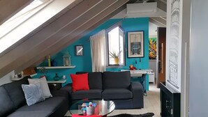 Ein modernes Wohnzimmer mit schrägverdeckter Decke, einer schwarzen Couch, einem Glastisch und einem roten Akzentstuhl.