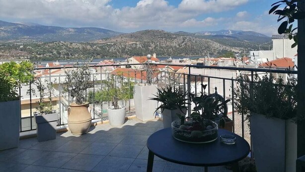 Ein Balkon mit Topfpflanzen, einem Tisch und Blick auf Stadt und Berge.