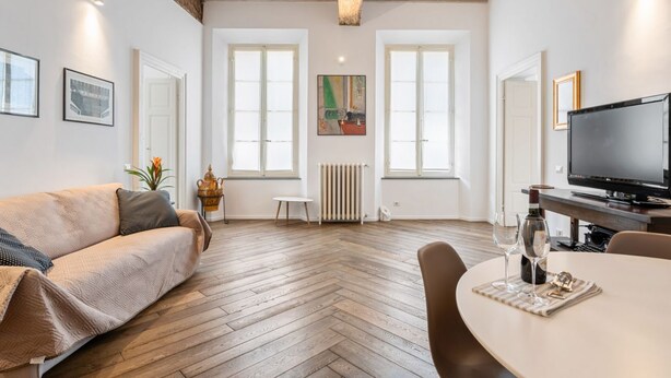 Un soggiorno moderno con pavimento in parquet a spina di pesce, un divano, un tavolo da pranzo con sedie, un televisore e opere d'arte alle pareti.