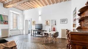 Un'ampia stanza con pavimento in legno, un tavolo da pranzo con sedie, una televisione e un armadio in legno.