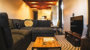 A compact living space with a sofa, a coffee table, a television, and a kitchen in the background. - Renovated 3BR LGD home near Magazine St. Walk to cafés, streetcar to FQ & Dome. (New Orleans)