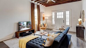A modern living room with a dark blue sofa, a television, and a wooden ceiling. - Renovated 3BR LGD home near Magazine St. Walk to cafés, streetcar to FQ & Dome. (New Orleans)