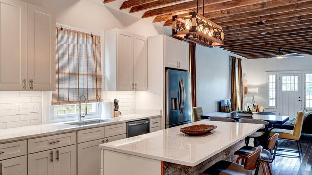 A modern kitchen with white cabinets, a marble island, and a wooden ceiling. - Renovated 3BR LGD home near Magazine St. Walk to cafés, streetcar to FQ & Dome. (New Orleans)