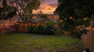 A backyard with a brick wall, wooden fence, and string lights.