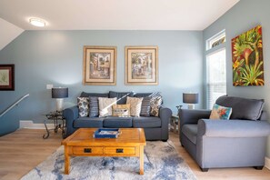 Sala de estar com um sofá azul, uma mesa de centro de madeira e duas pinturas emolduradas na parede.